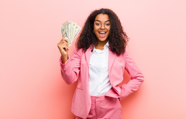 Giovane donna graziosa nera con le banconote del dollaro contro la parete rosa