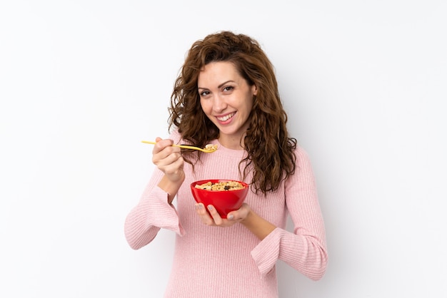 Giovane donna graziosa sopra la parete isolata che tiene una ciotola di cereali