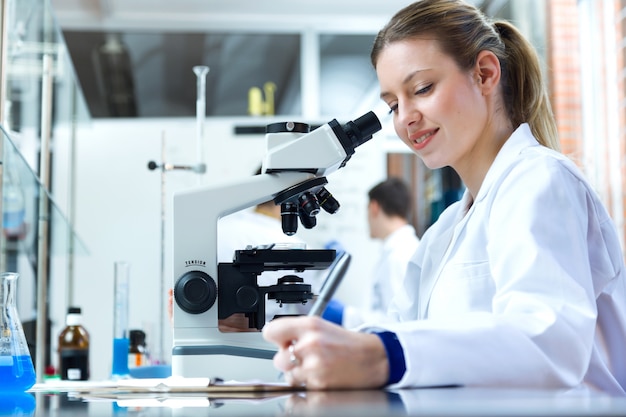 Giovane donna guardando attraverso il microscopio in laboratorio.