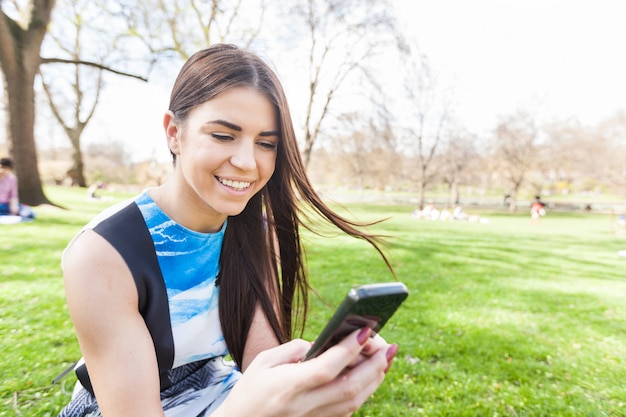 Giovane donna guardando smart phone al parco di Londra