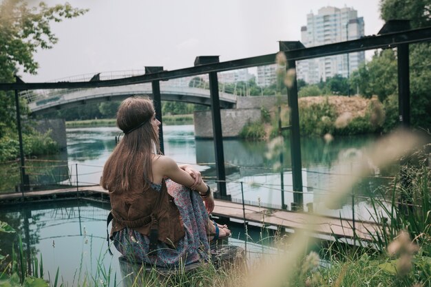 Giovane donna hippie seduta vicino a uno stagno cittadino. il concetto di unità con la natura