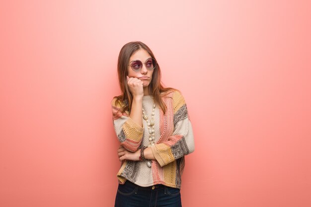 Giovane donna hippie su sfondo rosa pensando a qualcosa, guardando al lato