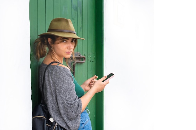 Giovane donna hipster che guarda dritto alla telecamera mentre tiene il suo smartphone e una sigaretta elettronica