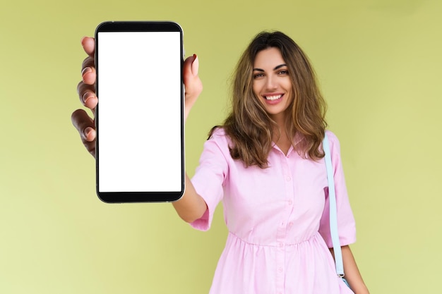 Giovane donna in abbigliamento casual isolato su sfondo verde tiene un telefono con uno schermo bianco vuoto
