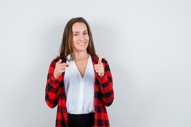 Giovane donna in abiti casual che punta alla telecamera e sembra gioviale, vista frontale.