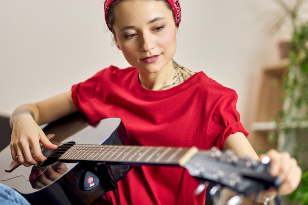 Giovane donna in abiti casual che sembra concentrata mentre suona la chitarra a casa