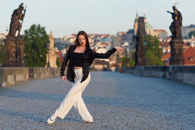 Giovane donna in abiti casual eleganti che ballano sul ponte di pietra della città vecchia in una praga attiva