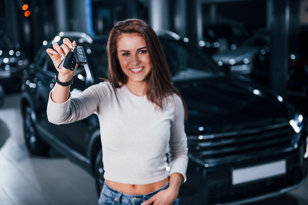 Giovane donna in abiti casual in piedi vicino alla moderna auto nera con le chiavi in mano.