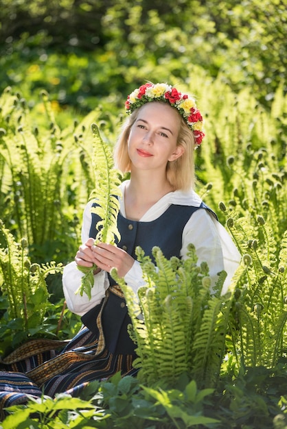 Giovane donna in abiti nazionali e corona contro una vacanza lettone ligo felce verde