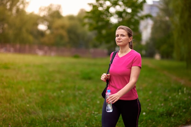 Giovane donna in abiti sportivi cammina nel parco con una bottiglia d'acqua