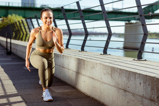 Giovane donna in abiti sportivi che si estende su una passeggiata sul fiume