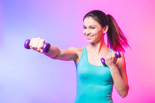 Giovane donna in abiti sportivi con un bel sorriso che tiene il manubrio del peso facendo allenamento fitness