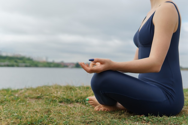 Giovane donna in abiti sportivi seduti in posa yoga, vista laterale, cielo nuvoloso sullo sfondo. Allenamento Yogi, meditazione all'aperto, stile di vita sano. avvicinamento