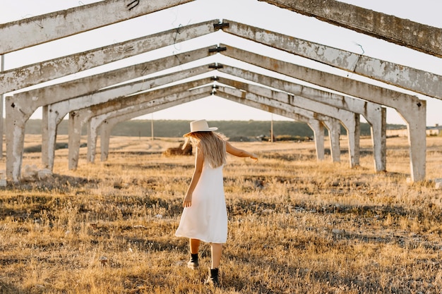 Giovane donna in abito bianco, camminando in campagna in un campo con erba secca
