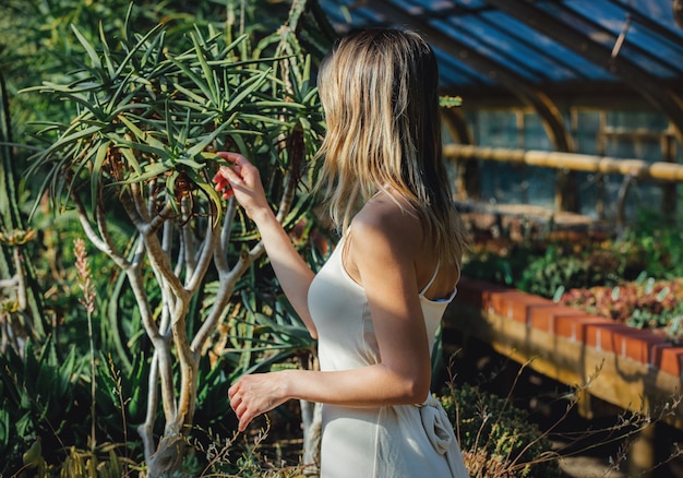 Giovane donna in abito bianco in serra con piante grasse