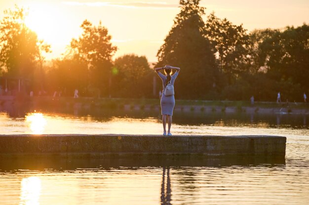 Giovane donna in abito casual rilassante sul lato del lago in una calda serata. Vacanze estive e concetto di viaggio.