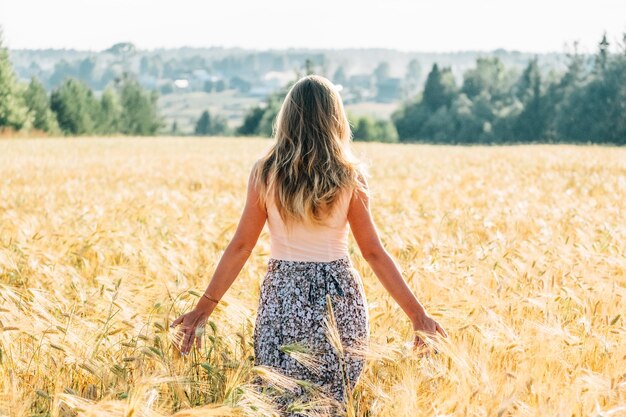 Giovane donna in abito che cammina lungo un campo di cereali