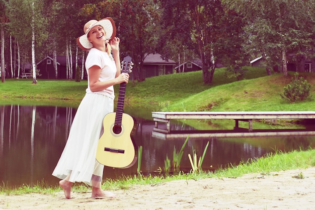 Giovane donna in abito con una chitarra sul lago