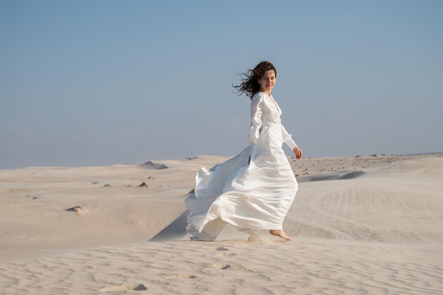Giovane donna in abito da sposa bianco che cammina sulle dune di sabbia nel deserto