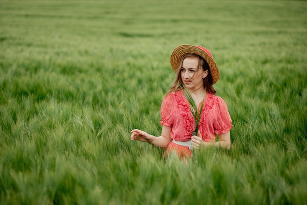 Giovane donna in abito e cappello in un campo di orzo