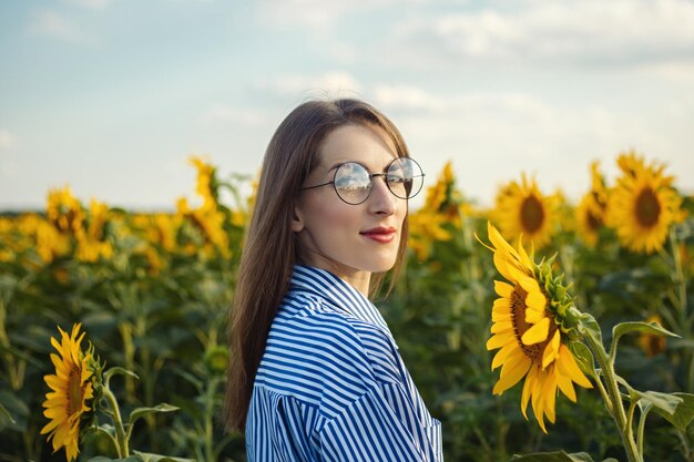 Giovane donna in abito e occhiali al tramonto su un campo di girasoli