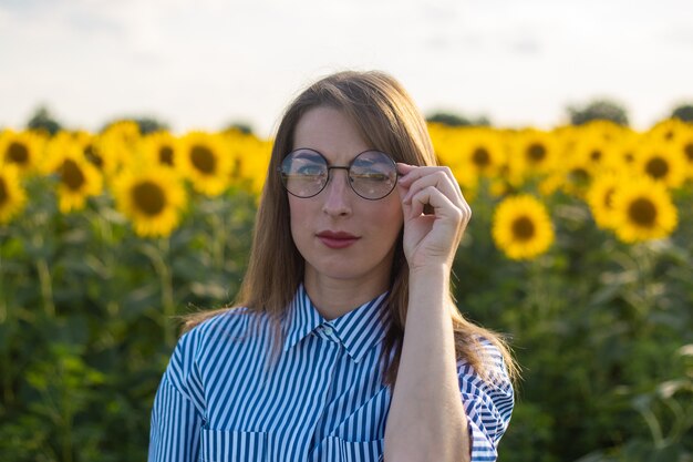 Giovane donna in abito e occhiali su un campo di girasoli.