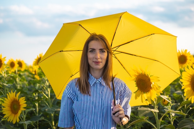 Giovane donna in abito e ombrello giallo sul campo di girasoli.