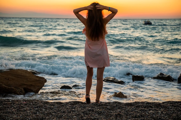 Giovane donna in abito estivo su sfondo tramonto in mare