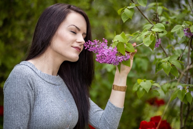 Giovane donna in abito grigio che odora un fiore lilla in estate