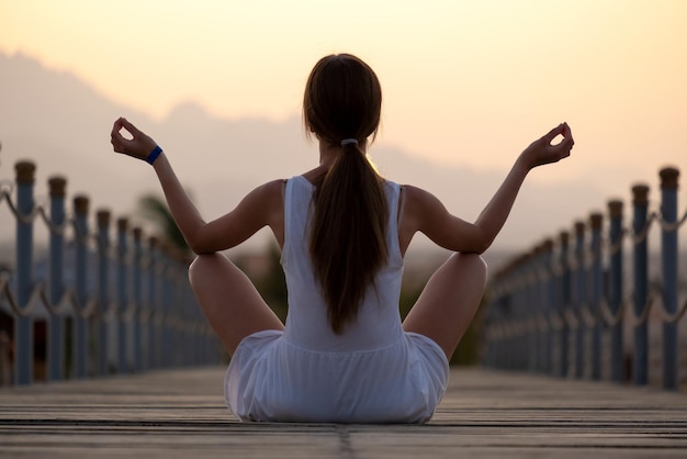 Giovane donna in abito leggero meditando sulla calda serata di sole sulla riva del mare. Vacanze estive e concetto di benessere.