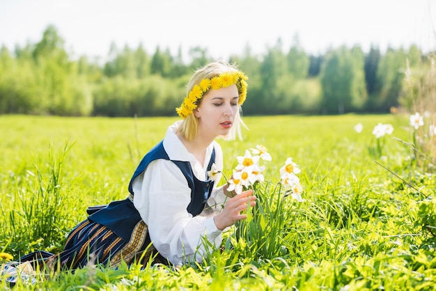 Giovane donna in abito nazionale in un campo con fiori di narcisi