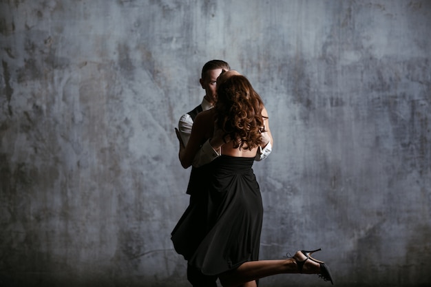 Giovane donna in abito nero e uomo danza tango