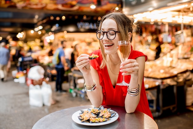 Giovane donna in abito rosso a pranzo con cozze e vino rosato seduti al mercato alimentare