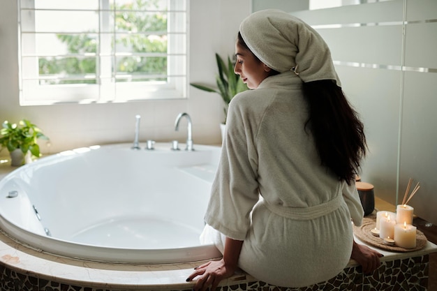 Giovane donna in accappatoio che si siede accanto al concetto di giorno a casa della vasca da bagno spa