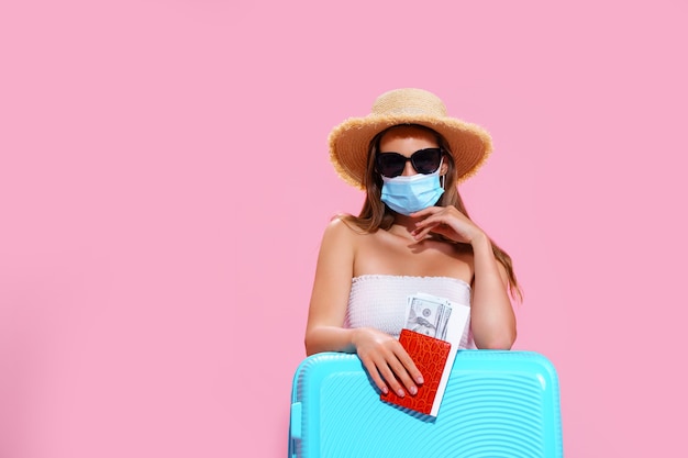 Giovane donna in attesa del volo seduta sul pavimento vicino alla sua valigia che indossa una maschera facciale per prevenire il coron...