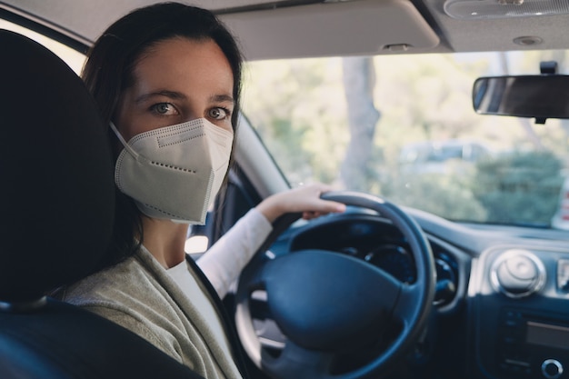 Giovane donna in auto che indossa una maschera protettiva durante la pandemia COVID-19