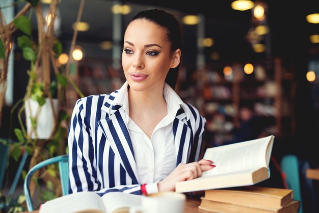 Giovane donna in biblioteca. Bere un caffè e leggere un libro. Rilassamento ed educazione, godendo del libro e del caffè.