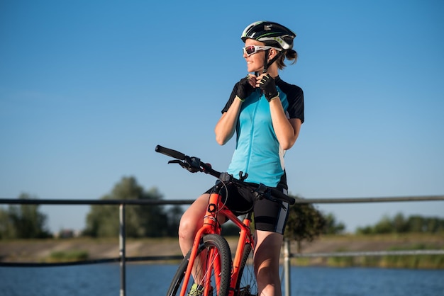 Giovane donna in bicicletta che indossa un casco sullo sfondo del cielo