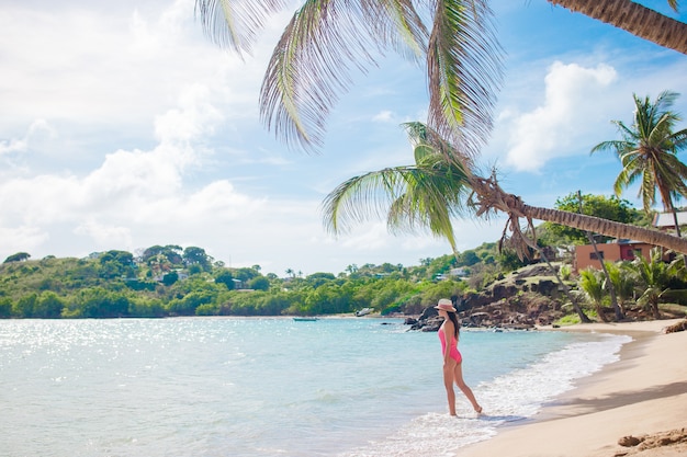 Giovane donna in bikini e cappello di paglia sulla spiaggia tropicale. La bella ragazza sotto la palma sulla spiaggia tropicale della baia di Carlisle con sabbia bianca e l'oceano del turchese innaffiano all'isola dell'Antigua nei Caraibi