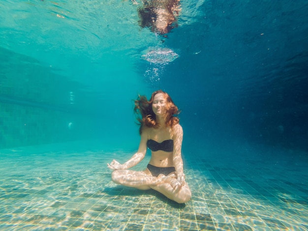 Giovane donna in bikini nero in posizione yoga sott'acqua in acquario subacqueo, colpo completo del corpo, vista frontale.