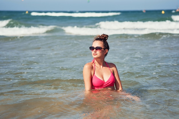 Giovane donna in bikini rosa che posa in un mare.