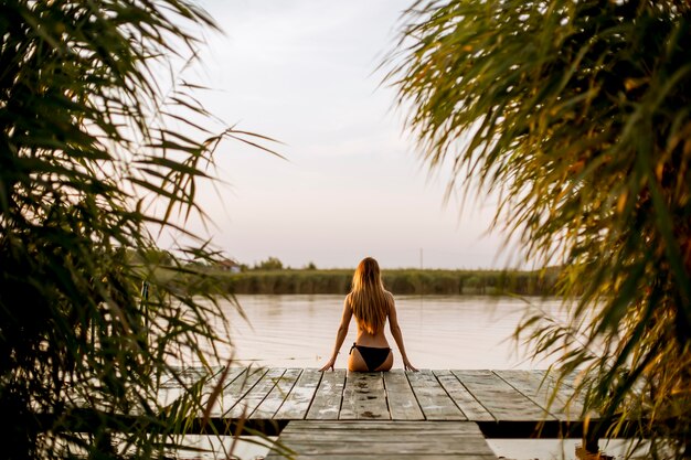 Giovane donna in bikini seduto su un molo sul lago