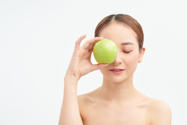 Giovane donna in buona salute che tiene mela verde sopra i suoi occhi sul muro bianco