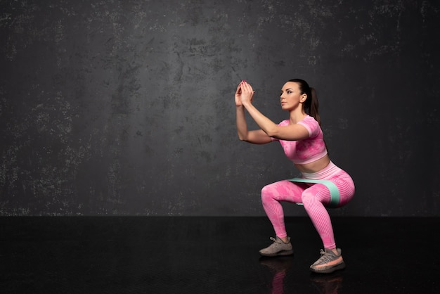 Giovane donna in buona salute di forma fisica che fa gli esercizi sopra fondo nero. Esercizi con un elastico. Sport e stile di vita sano