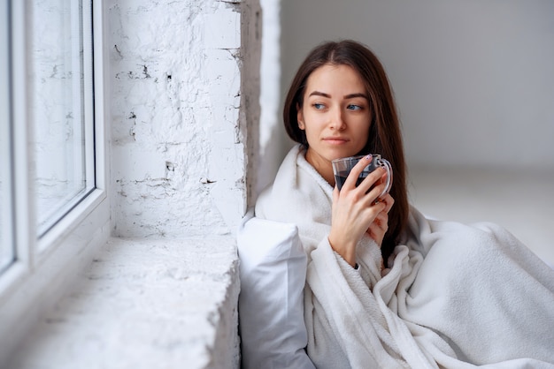 giovane donna in caldo plaid con calda tazza di tè nelle mani