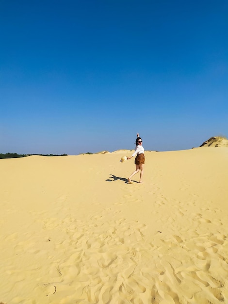 Giovane donna in camicetta bianca e pantaloncini marroni che cammina nel deserto