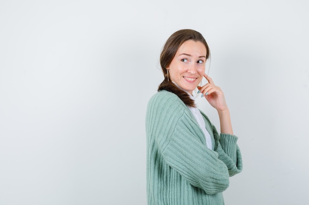 Giovane donna in camicetta, cardigan che tiene il dito sulla guancia, distoglie lo sguardo e sembra gioviale.