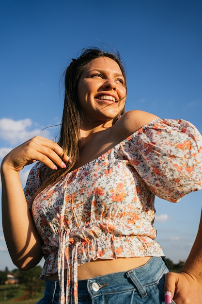 Giovane donna in camicetta fiorita sorridente all'aperto.