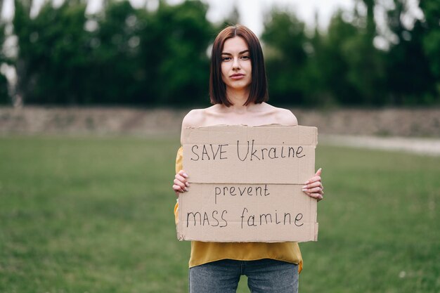 Giovane donna in camicetta gialla con poster in mano salva l'Ucraina