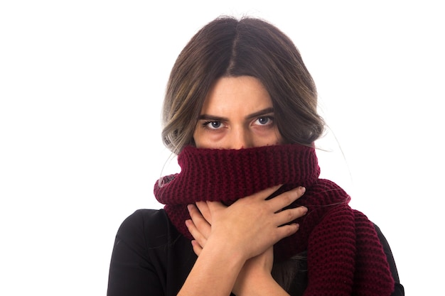 Giovane donna in camicetta nera che nasconde il viso con la sua lunga sciarpa rossa su sfondo bianco in studio